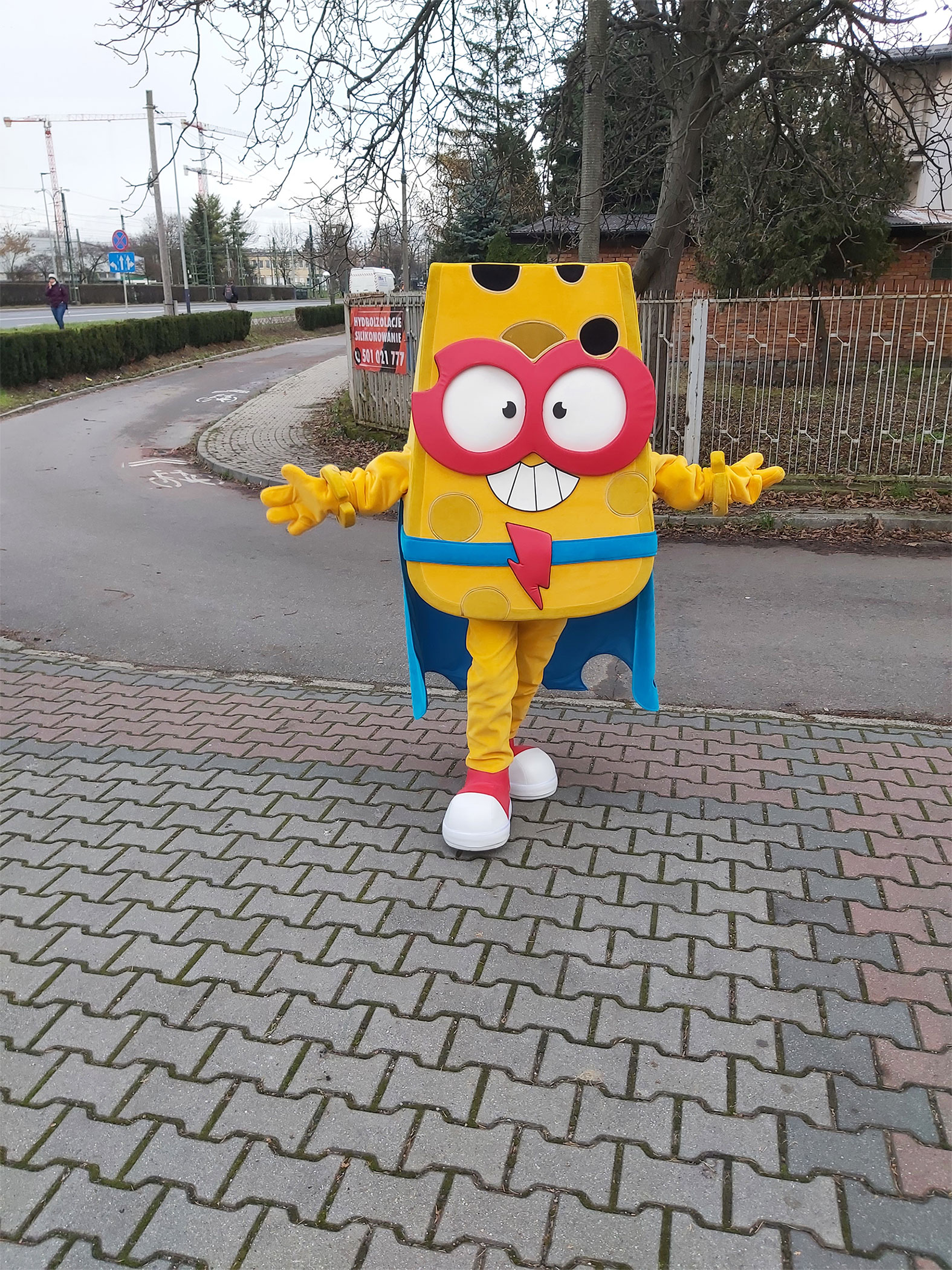Na fotografii widnieje strój reklamowy w postaci figurki SuperZings pozujący do zdjęcia przed siedzibą firmy Elabika 